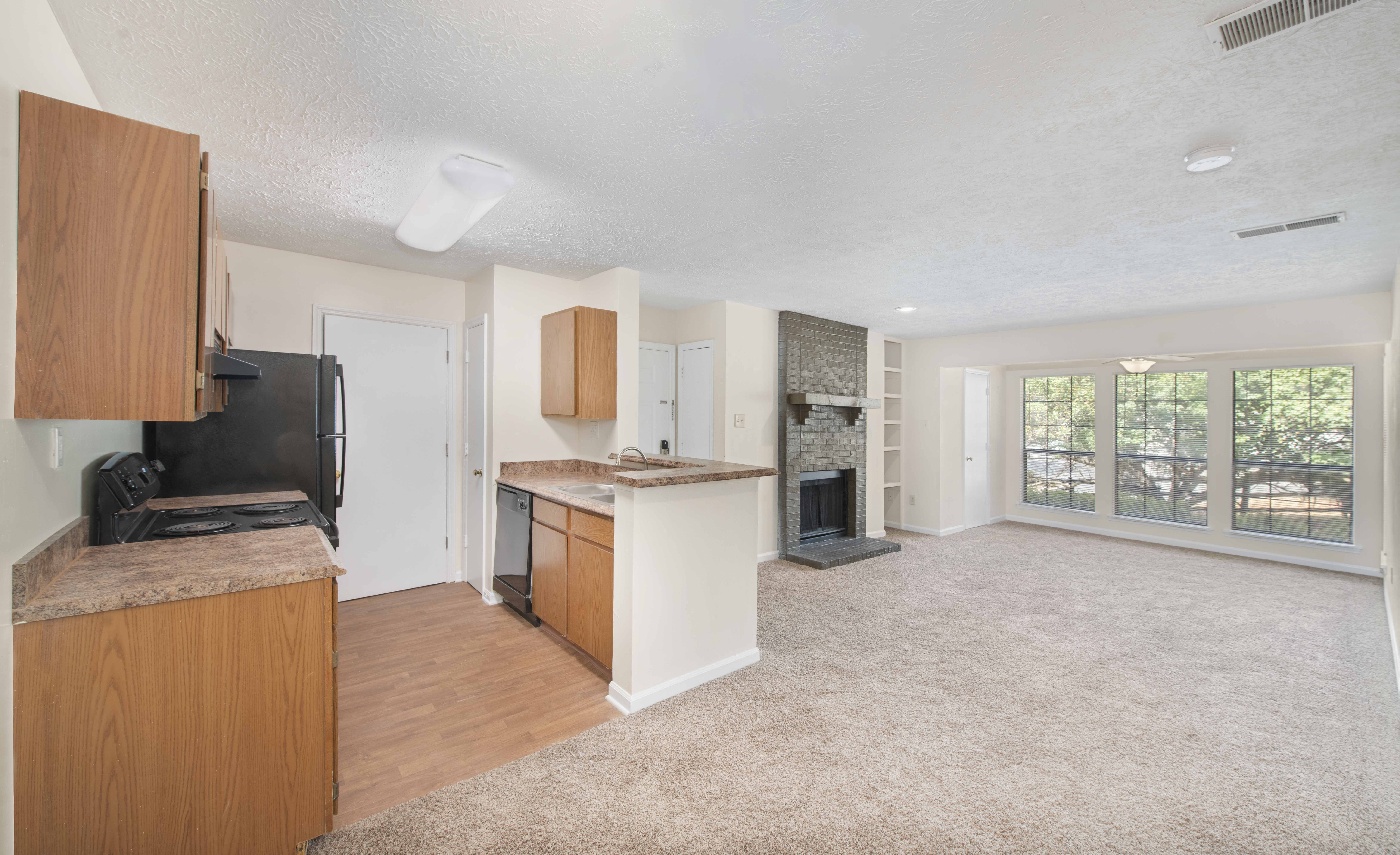 an empty living room with a kitchen and a fireplace