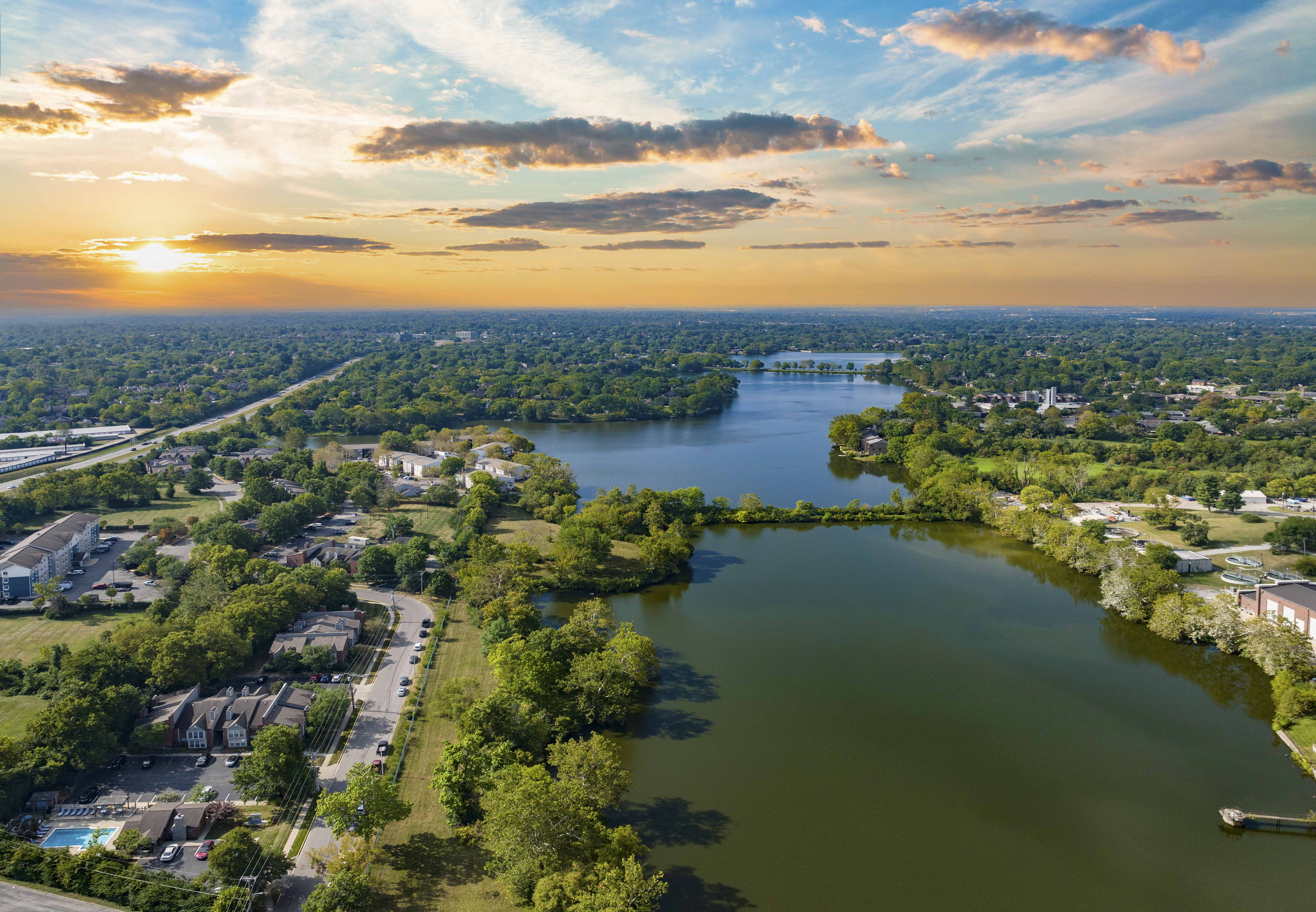an aerial view of a lake in a city with trees and a sunset