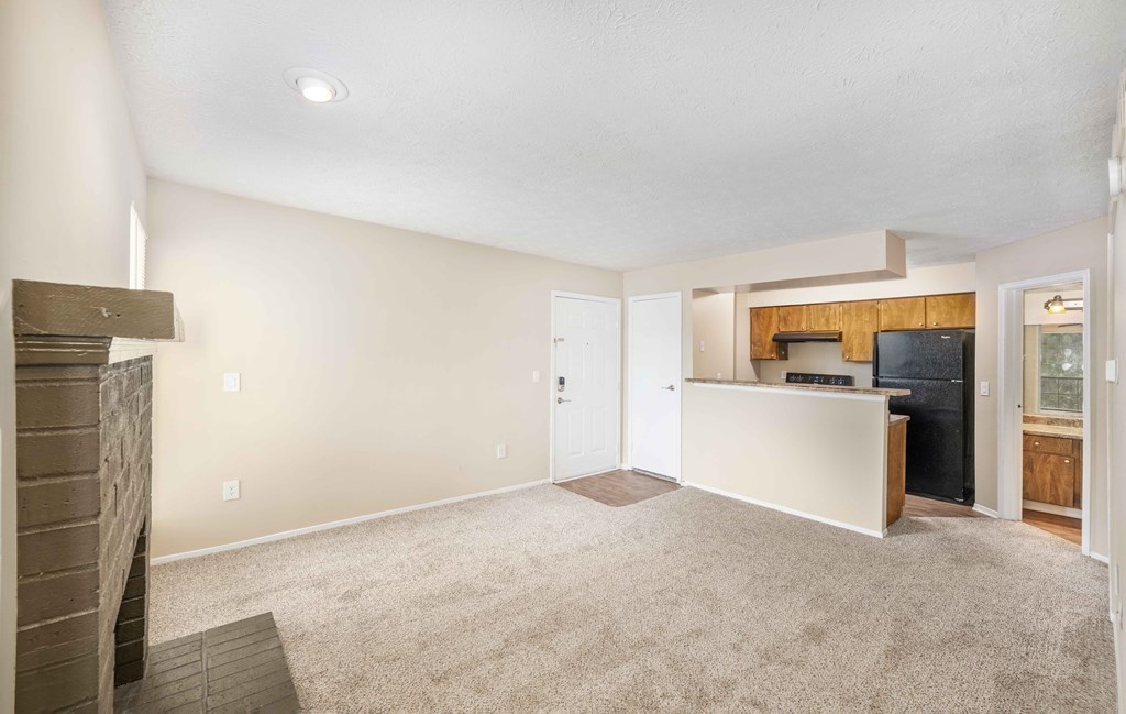 an empty living room with a fireplace and a kitchen