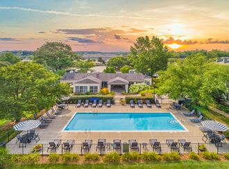 an aerial view of a pool with chairs and a house in the background at sunset