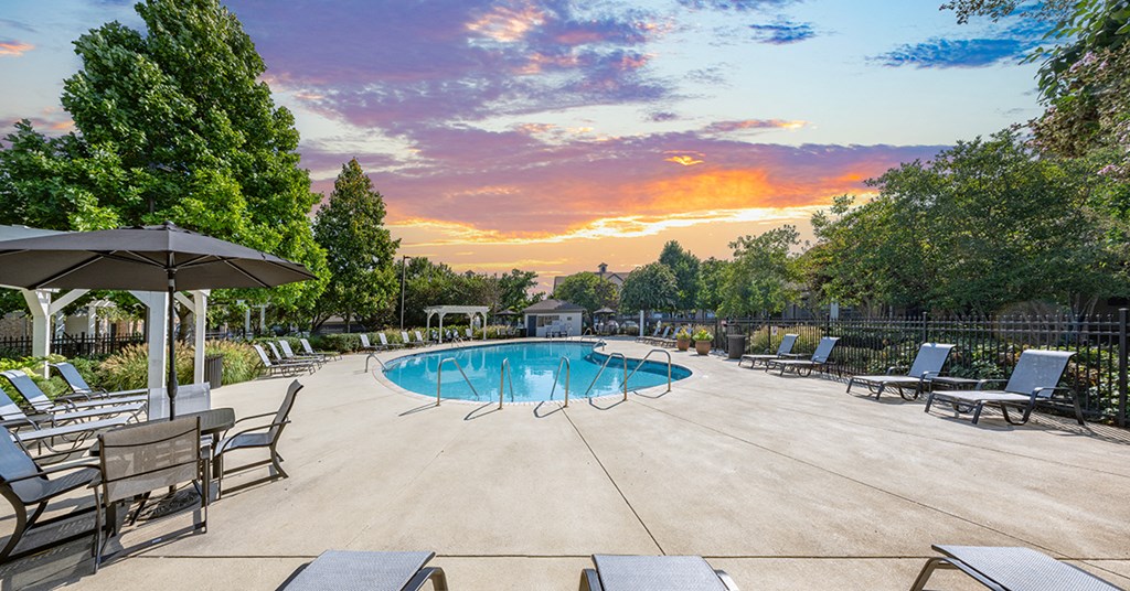 A sunset view of a pool area with lounge chairs and umbrellas.