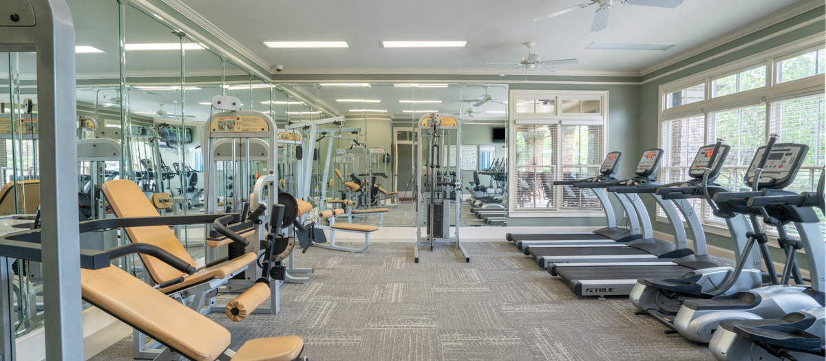 a gym with cardio equipment and weights in a building with windows