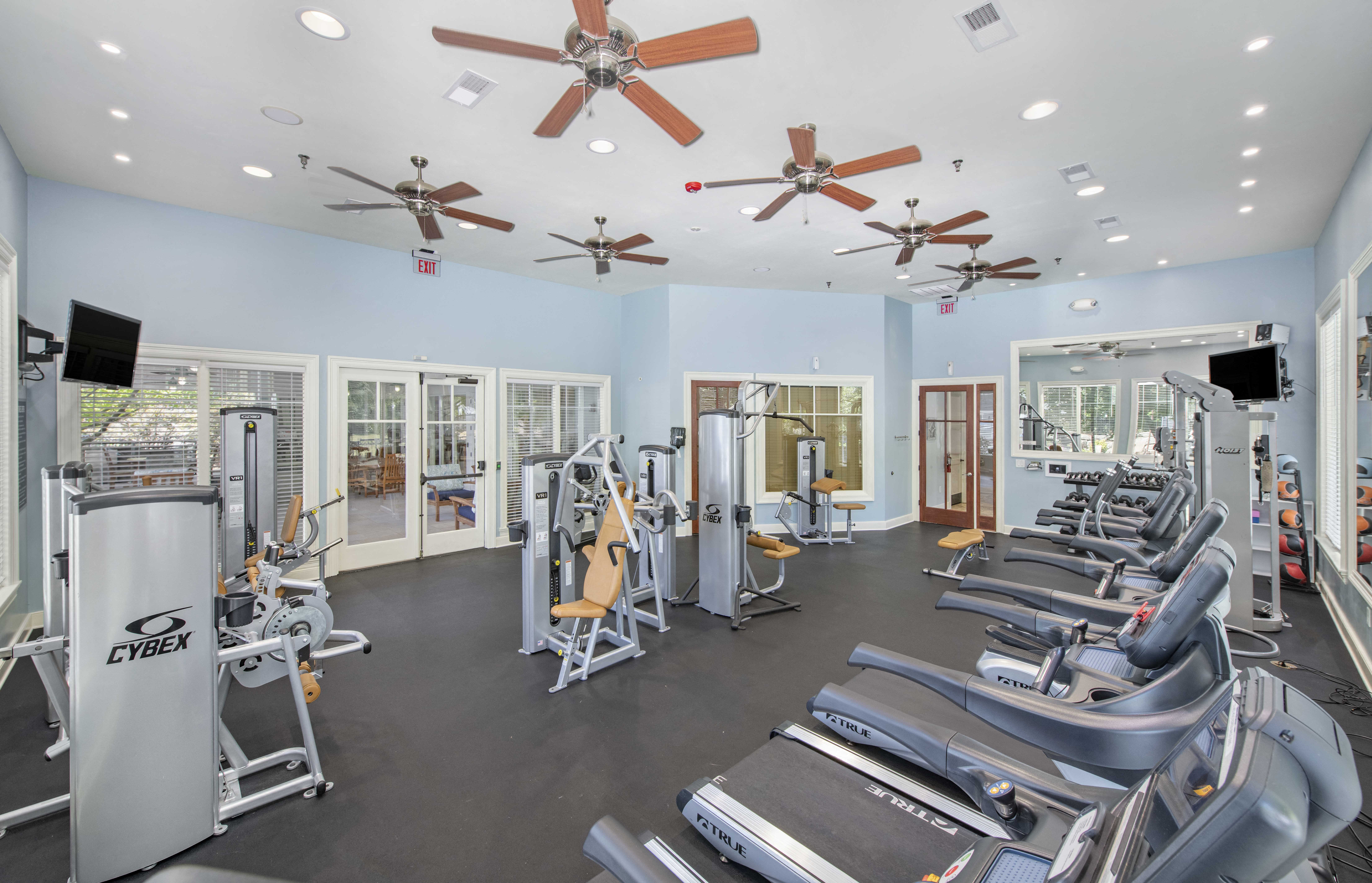 a gym with cardio equipment and ceiling fans