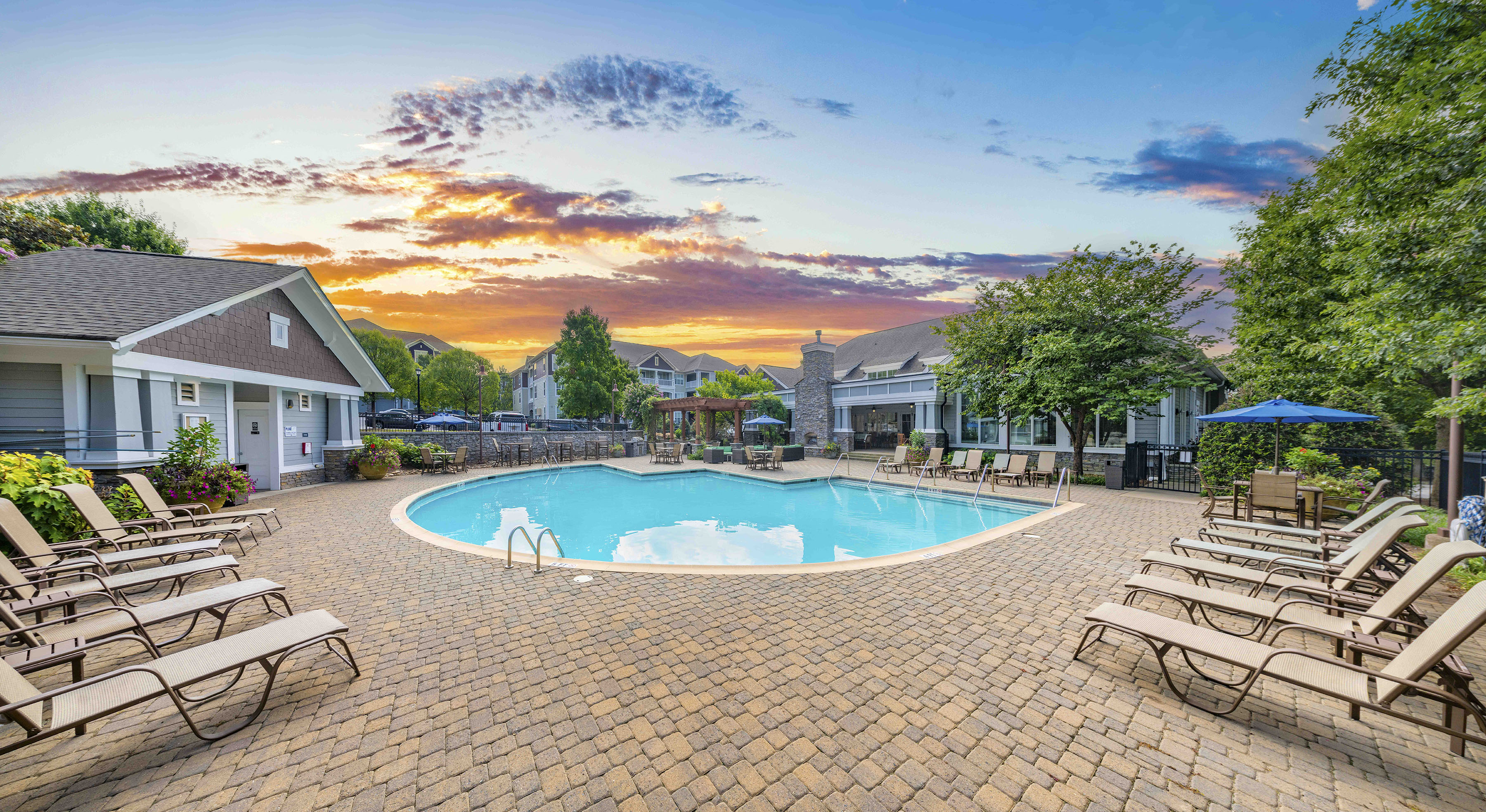 a pool with chairs and a house with a sunset in the background