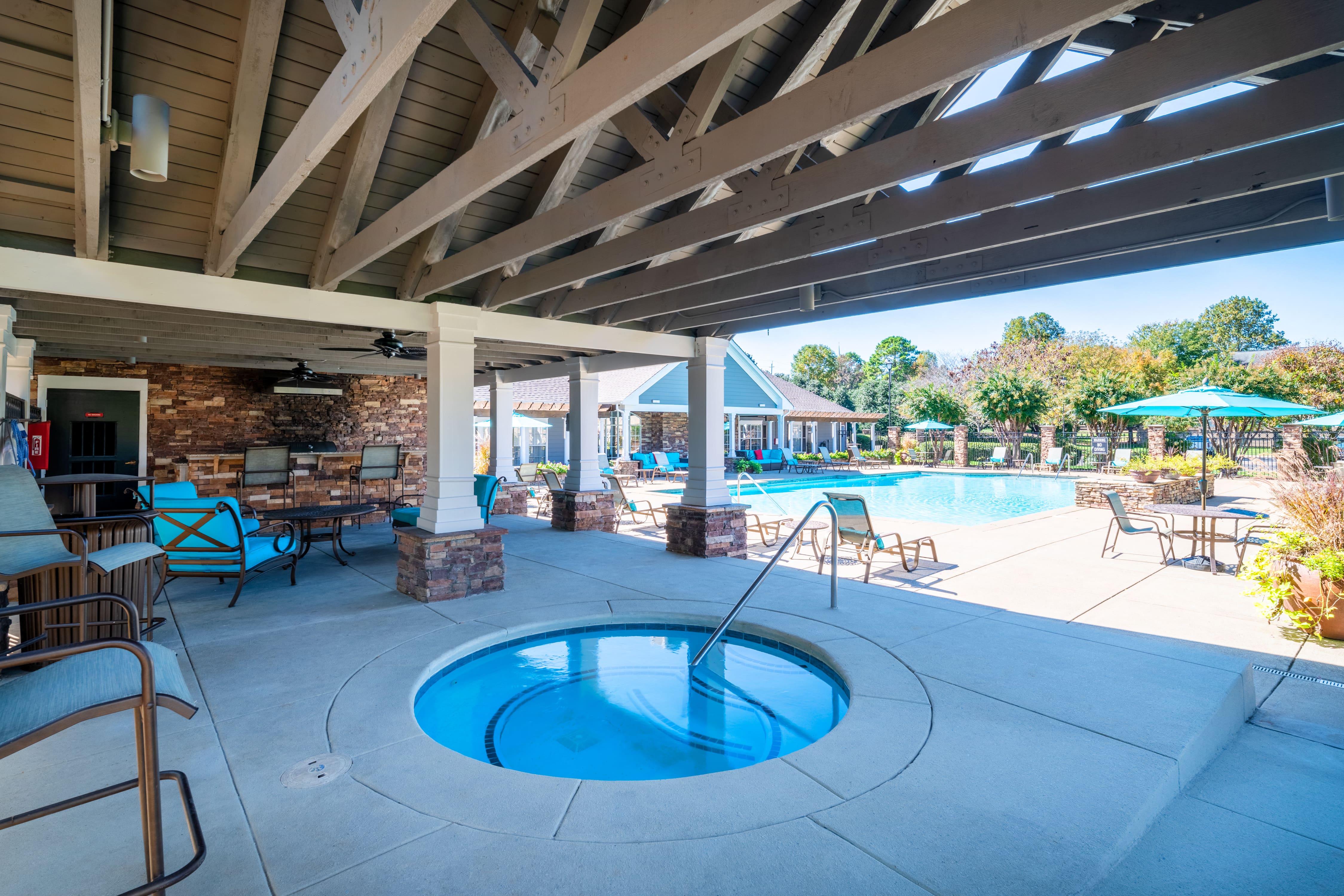 the pool is under a covered patio with chairs and a hot tub