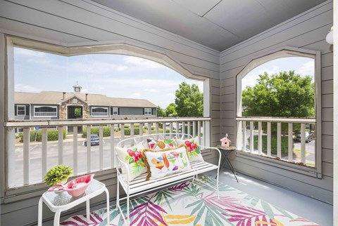 A white chair with a colorful cushion is on a porch.