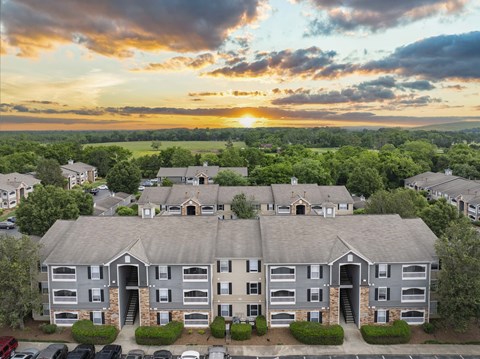 A sunset view of a large apartment complex with a parking lot in front.
