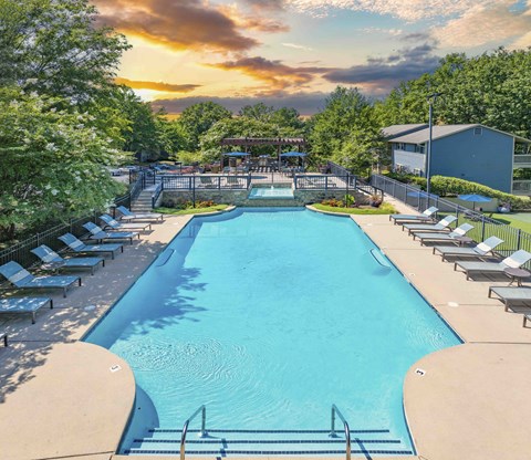 A large outdoor swimming pool surrounded by sun loungers and trees.