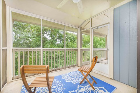A balcony with a blue rug and two wooden chairs.