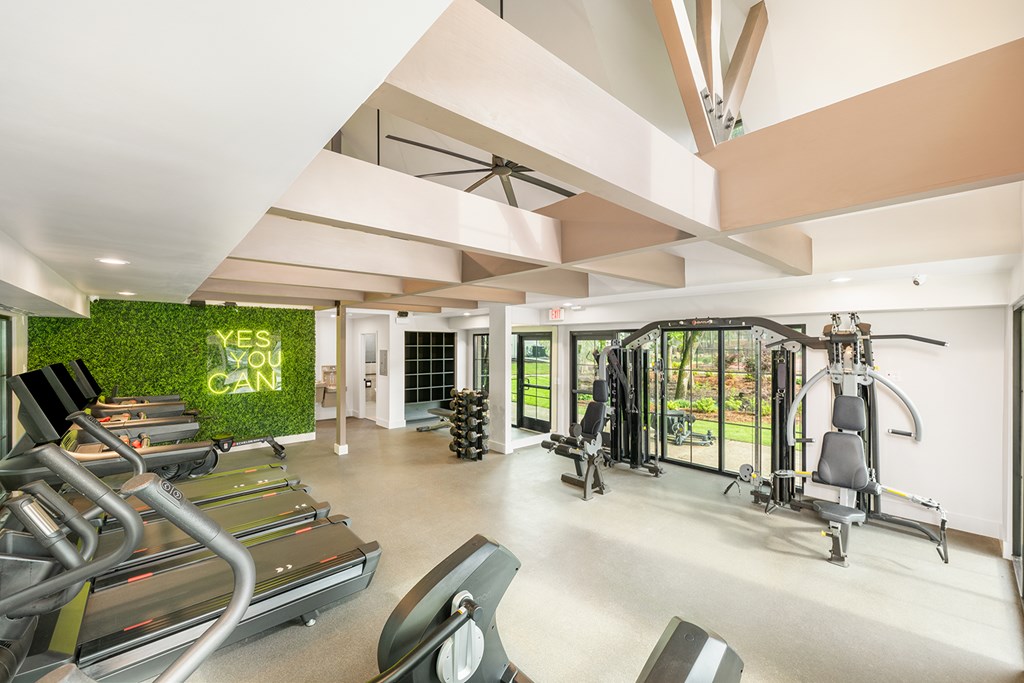 A gym with treadmills, weights and a green wall with the words "Yes You Can" on it.