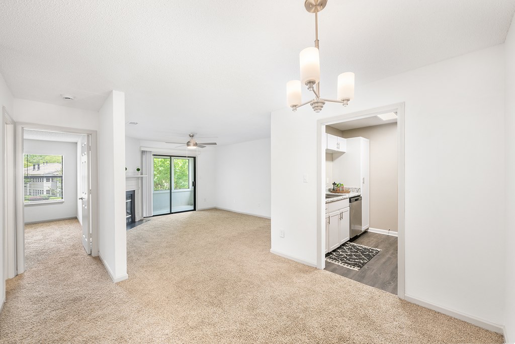 A spacious living room with a chandelier and a sliding glass door leading to a balcony.
