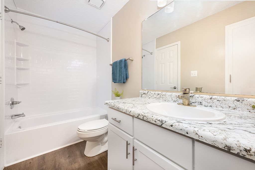 A white bathroom with a marble counter top and a white toilet.