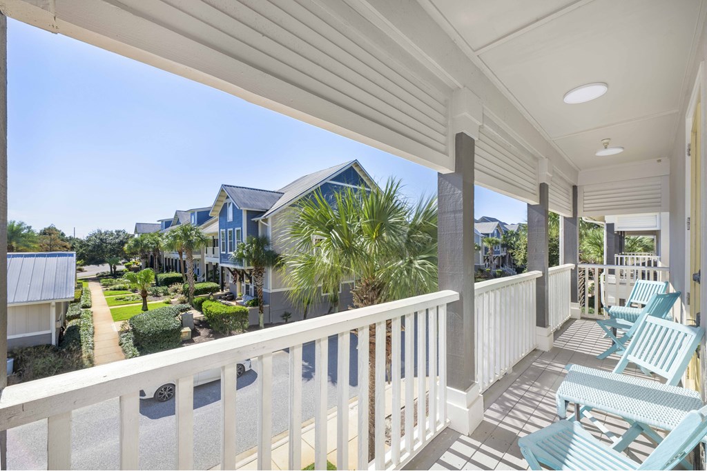 A white balcony with a white railing and a white ceiling with a view of a street and houses.