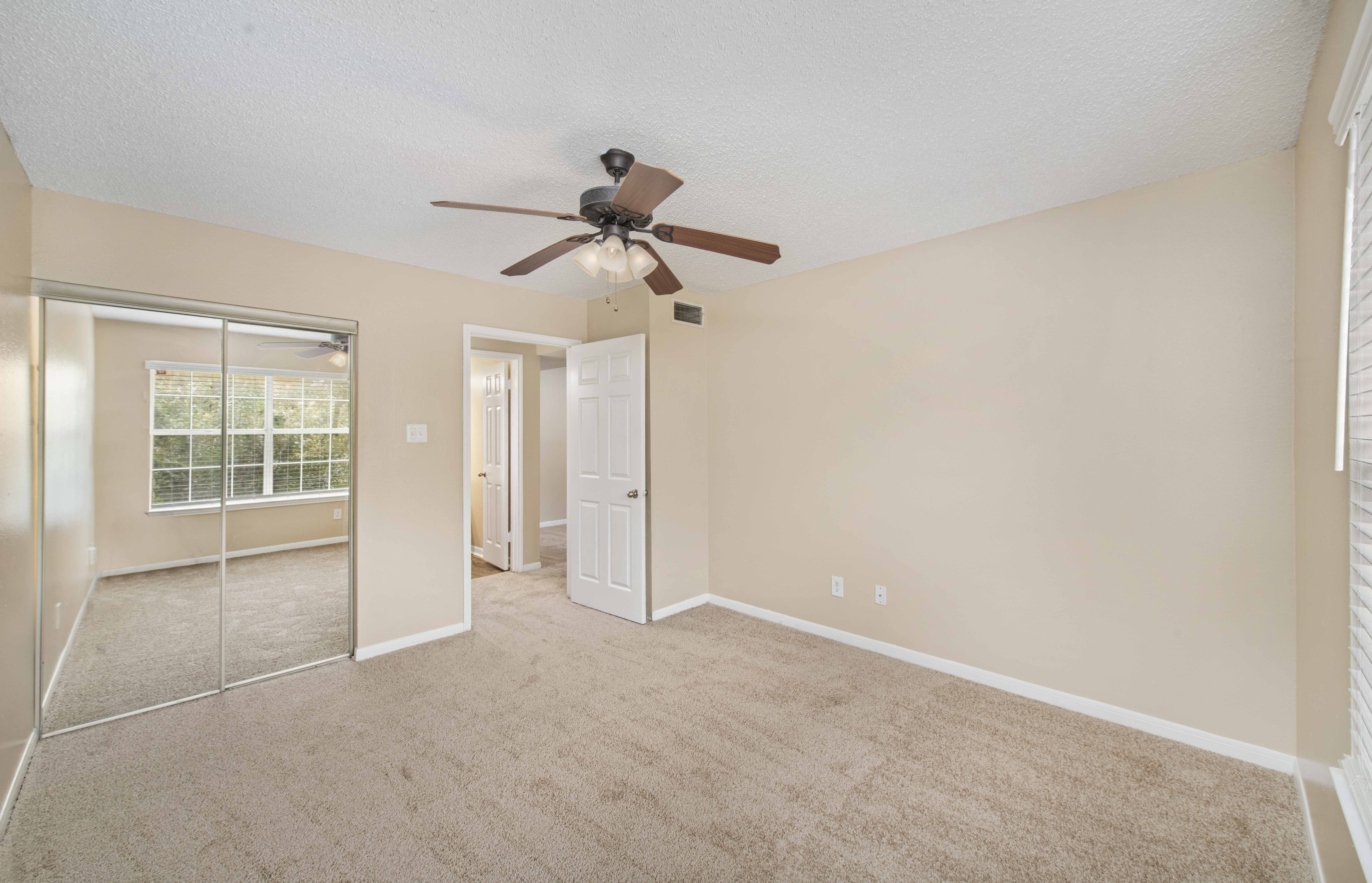 an empty living room with a ceiling fan and a mirrored closet