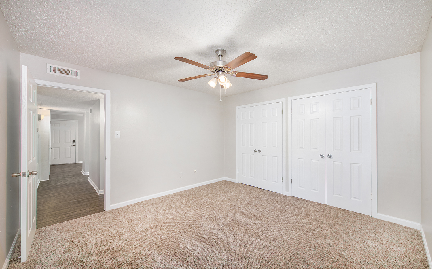 an empty bedroom with a ceiling fan and white closets