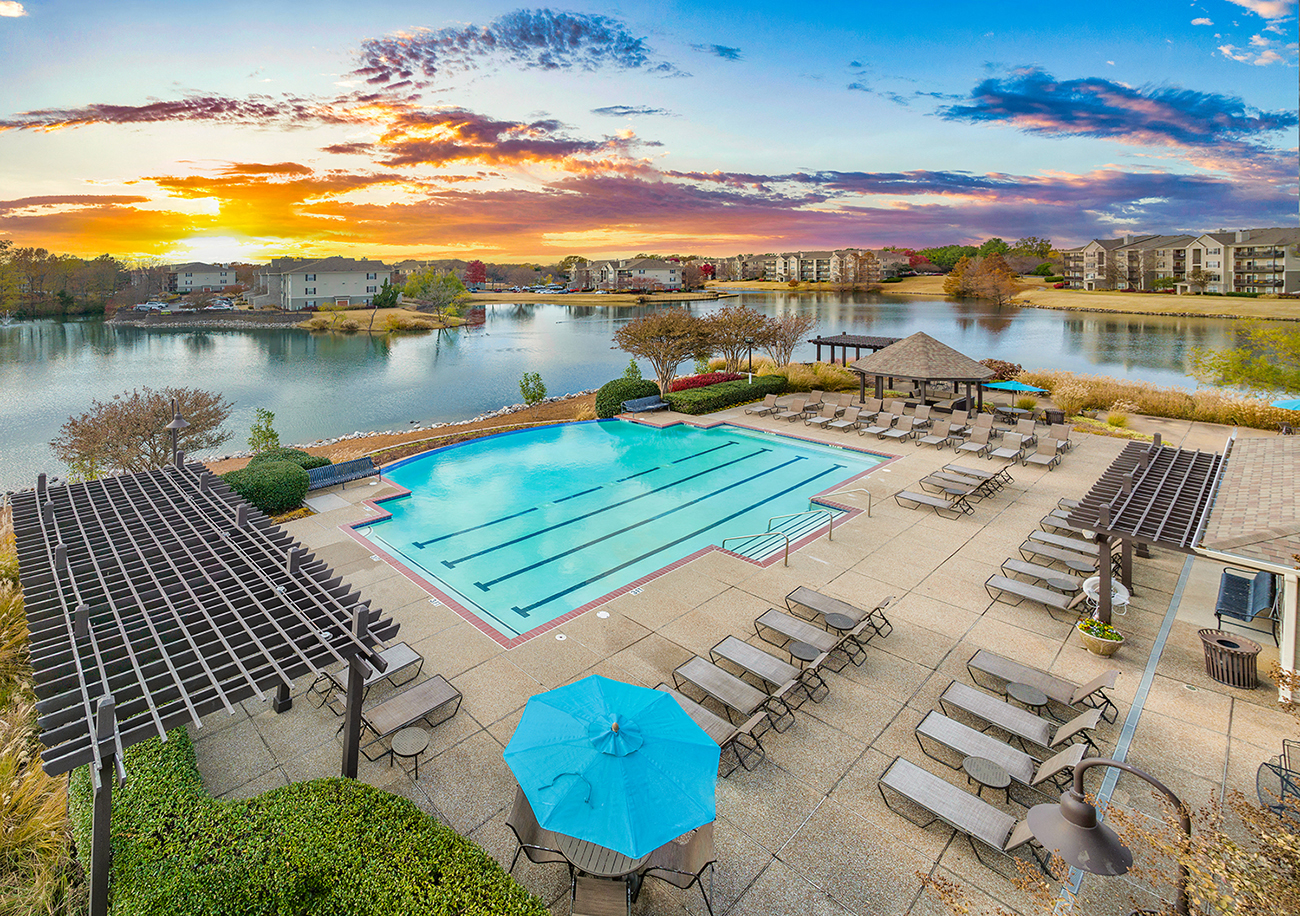 an aerial view of a pool with chairs and umbrellas at sunset