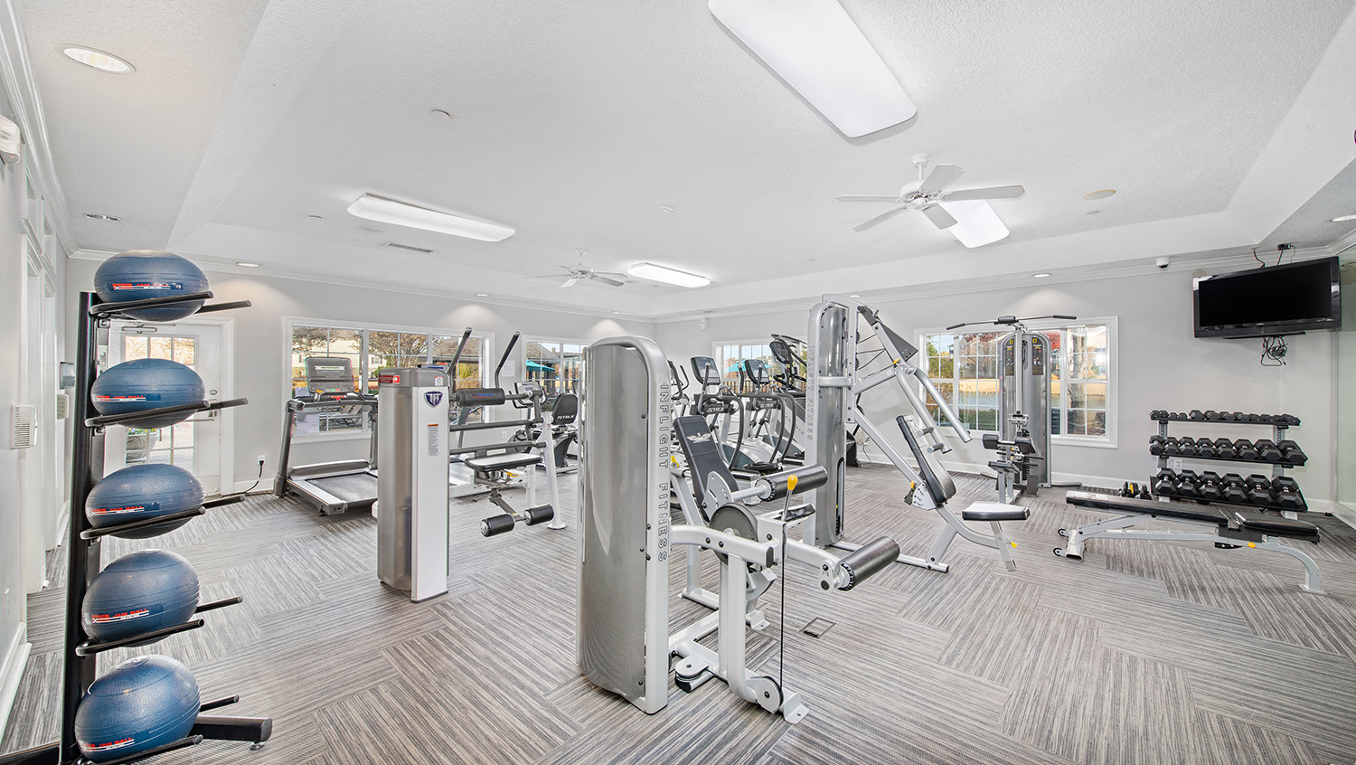 a gym with weights and cardio equipment on the floor and a tv