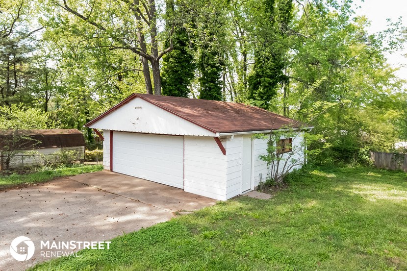 a small white shed in a yard with a concrete driveway