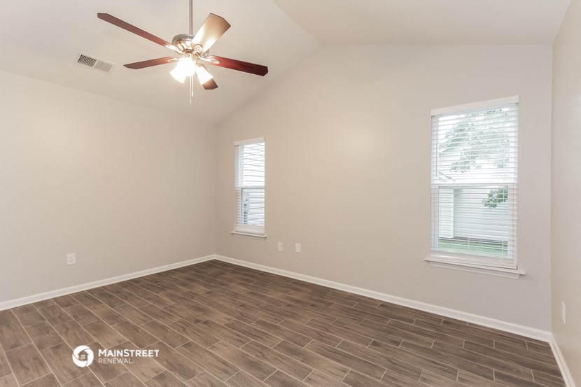 the spacious living room with wood flooring and a ceiling fan
