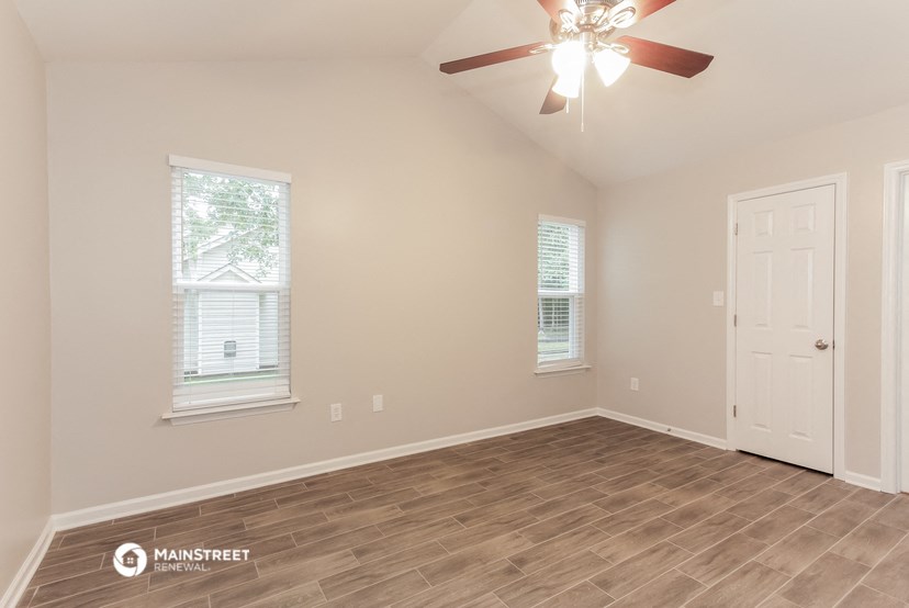 the spacious living room with hardwood flooring and a ceiling fan