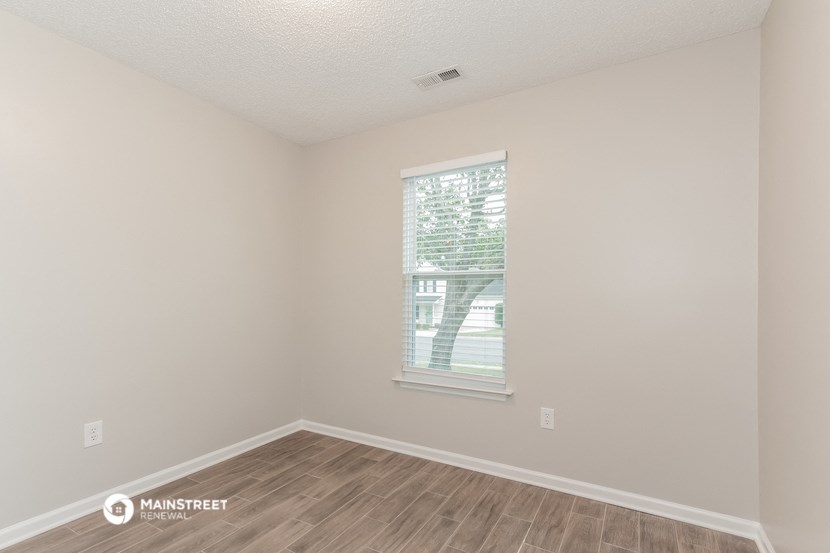 a spacious living room with a window and wood flooring