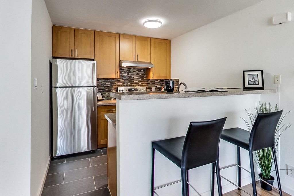 a kitchen with a bar with two stools and a refrigerator