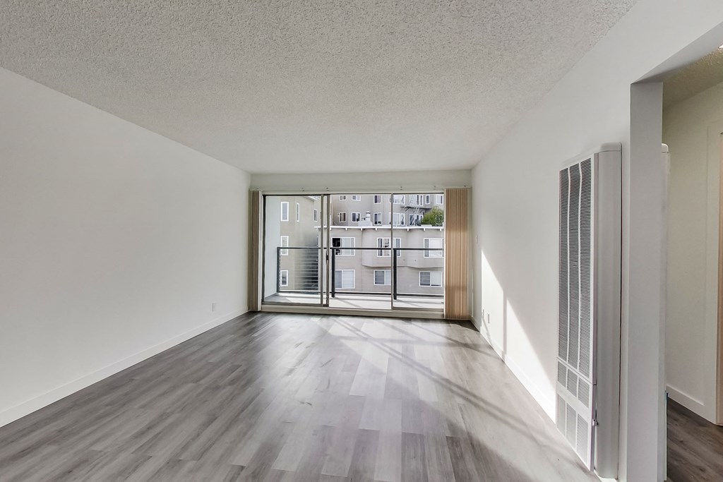 an empty living room with a sliding glass door to a balcony