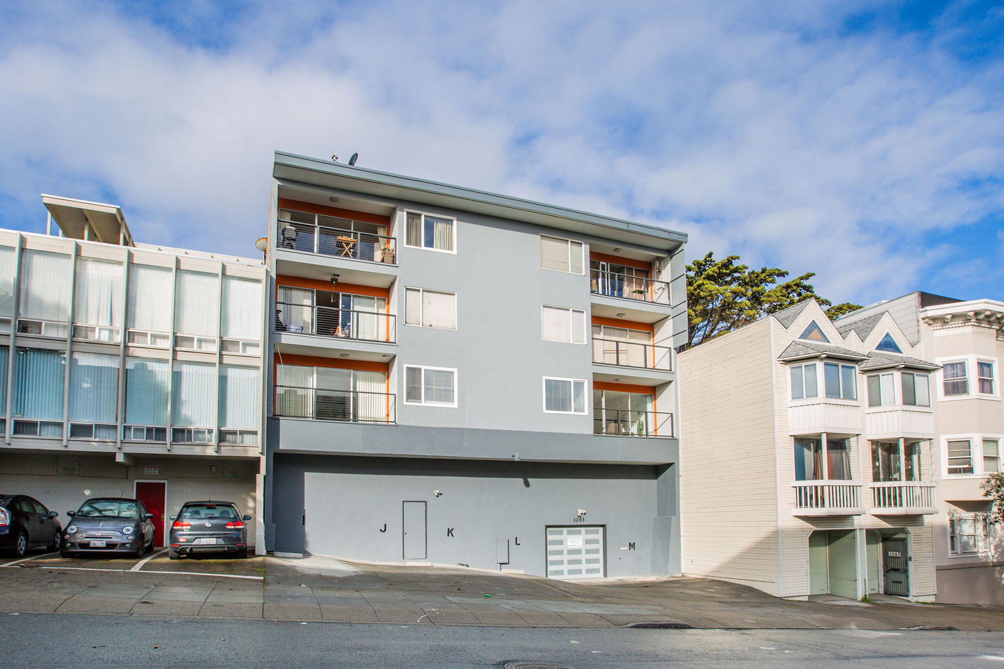 A grey apartment building with a parking lot in front.