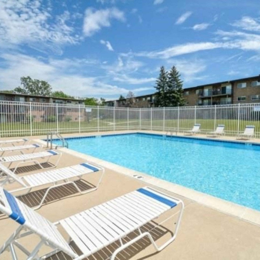 an outdoor pool with lounge chairs and a fence around it