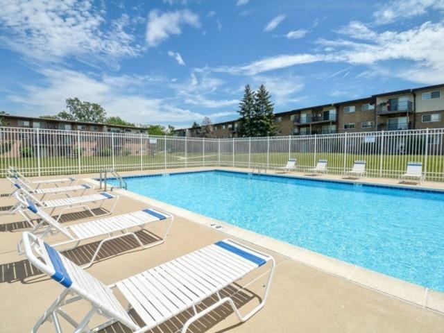 a swimming pool with chairs in front of an apartment building