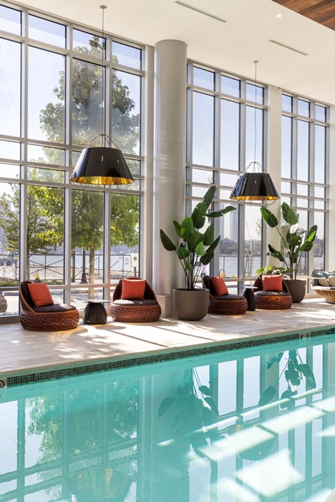 a swimming pool with chairs and potted plants in front of a window