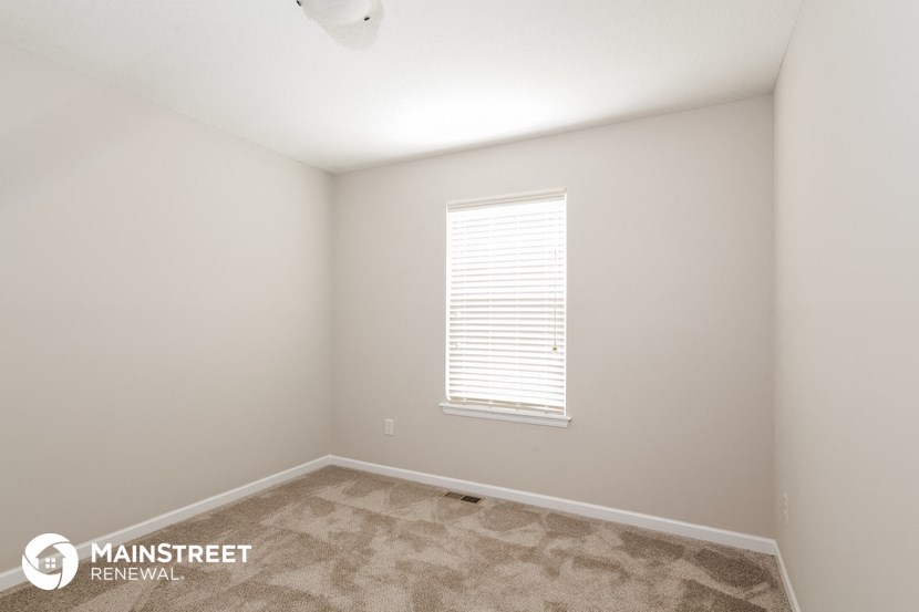 the bedroom of an apartment with carpet and a window