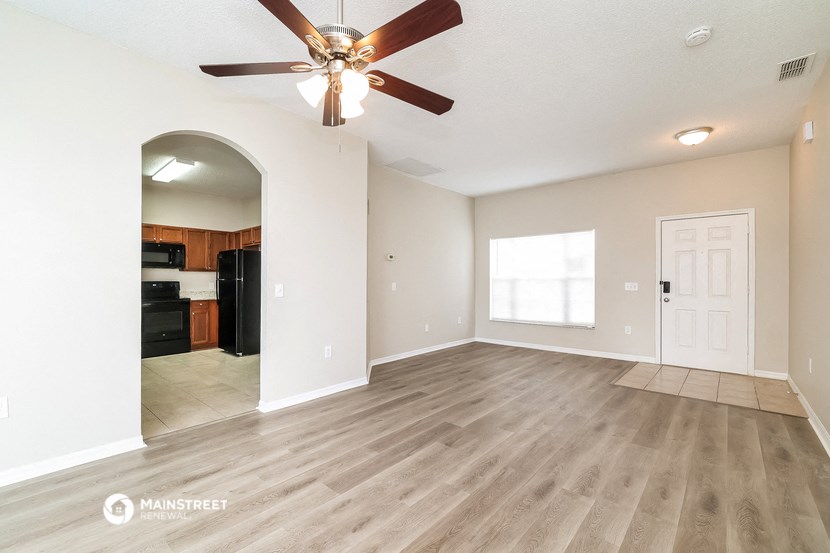 an empty living room with a ceiling fan and a kitchen