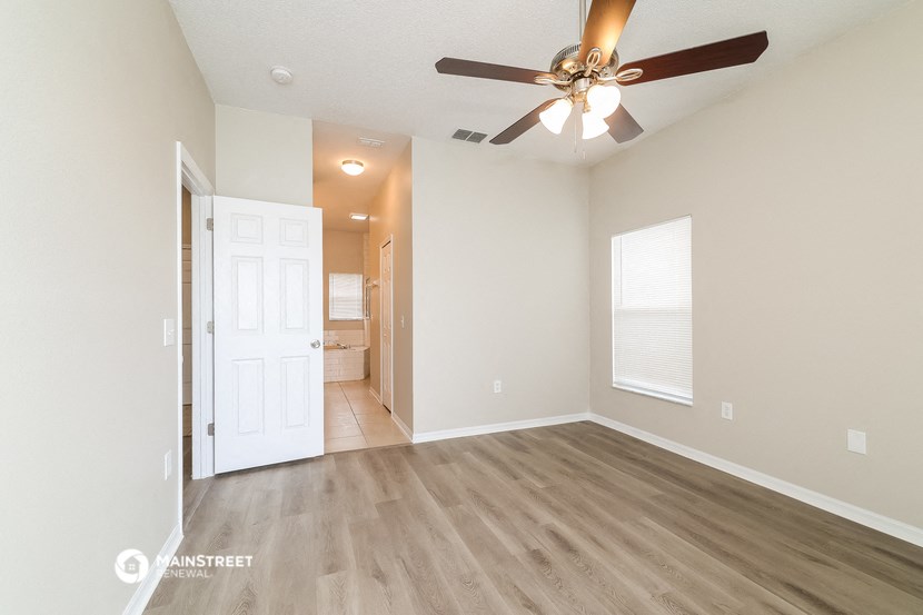 an empty living room with a ceiling fan and a door to a bathroom