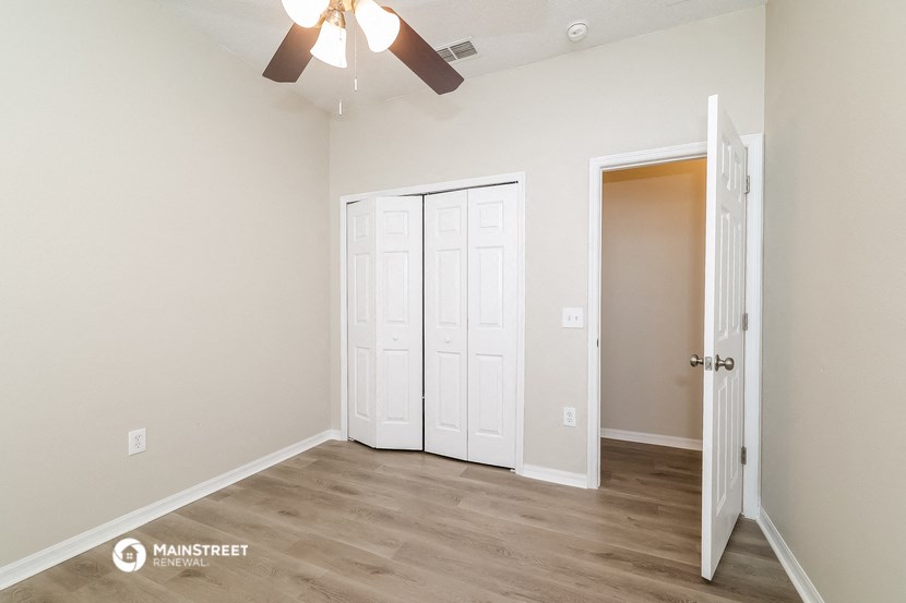 the living room of an apartment with white walls and a ceiling fan