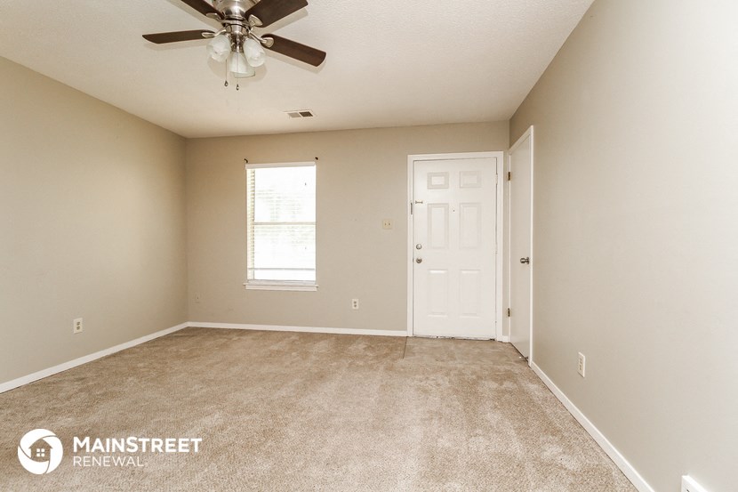 an empty living room with a ceiling fan and a white door