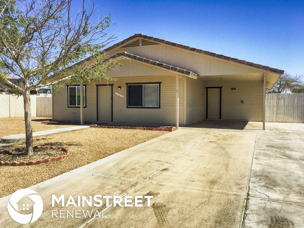 a small tan house with a driveway and a tree