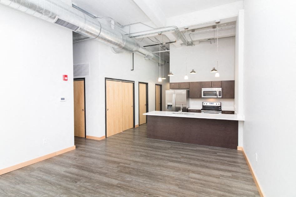 an empty living room with a kitchen and exposed ceilings