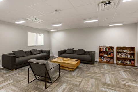 A room with grey couches, a coffee table, and a bookshelf.