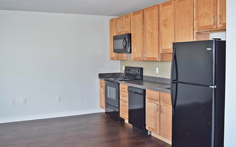 A black refrigerator is in the corner of a kitchen with wooden cabinets.