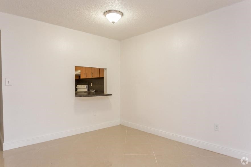 an empty living room with a kitchen in the corner