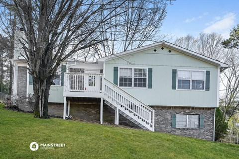 a white and green house with a deck on a hill