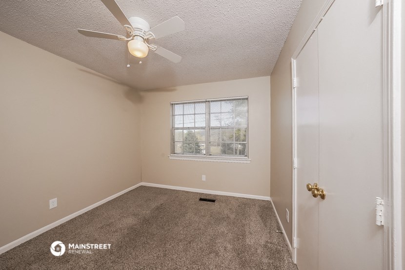 the spacious bedroom has a ceiling fan and carpeted flooring
