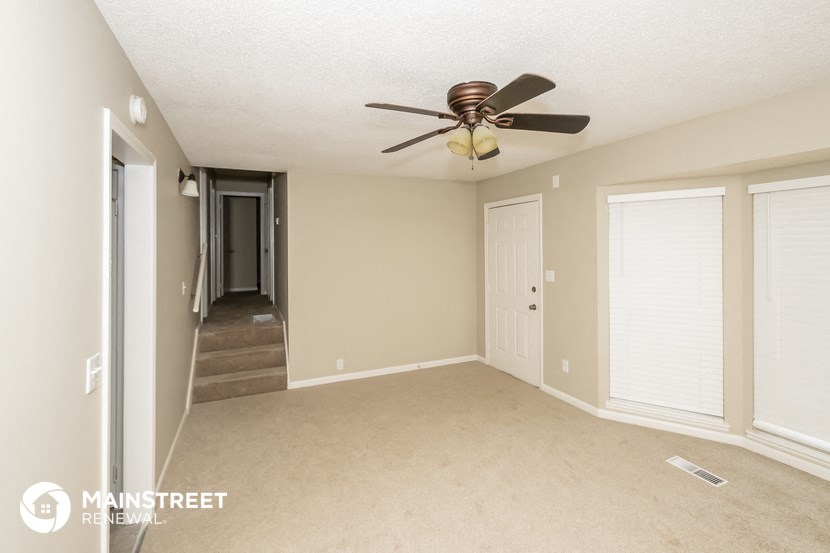 a living room with a ceiling fan and a door to a hallway
