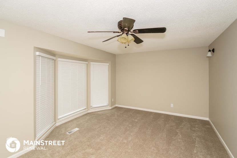 the spacious living room with ceiling fan and large windows