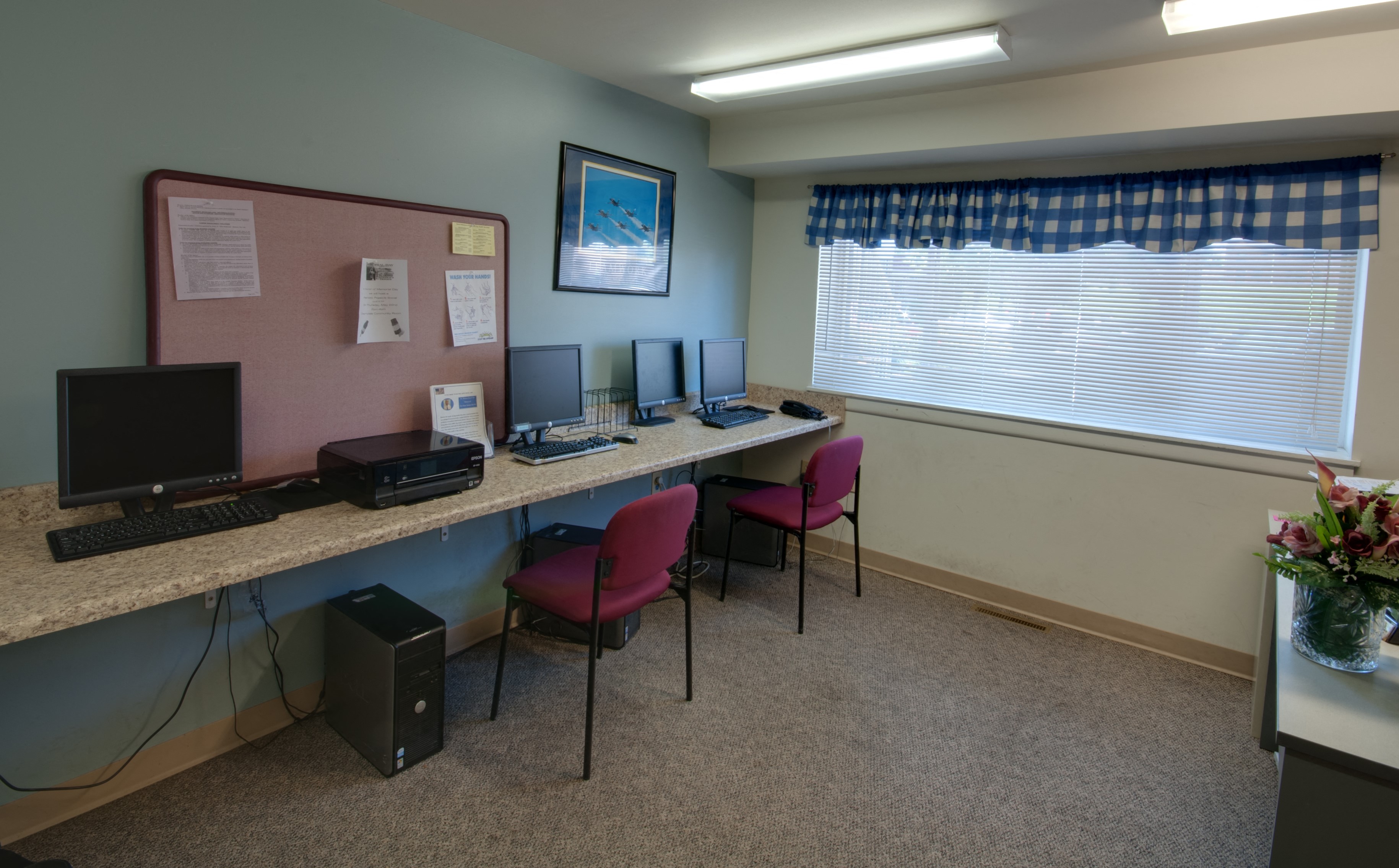 a computer room with three computers on a long desk with chairs