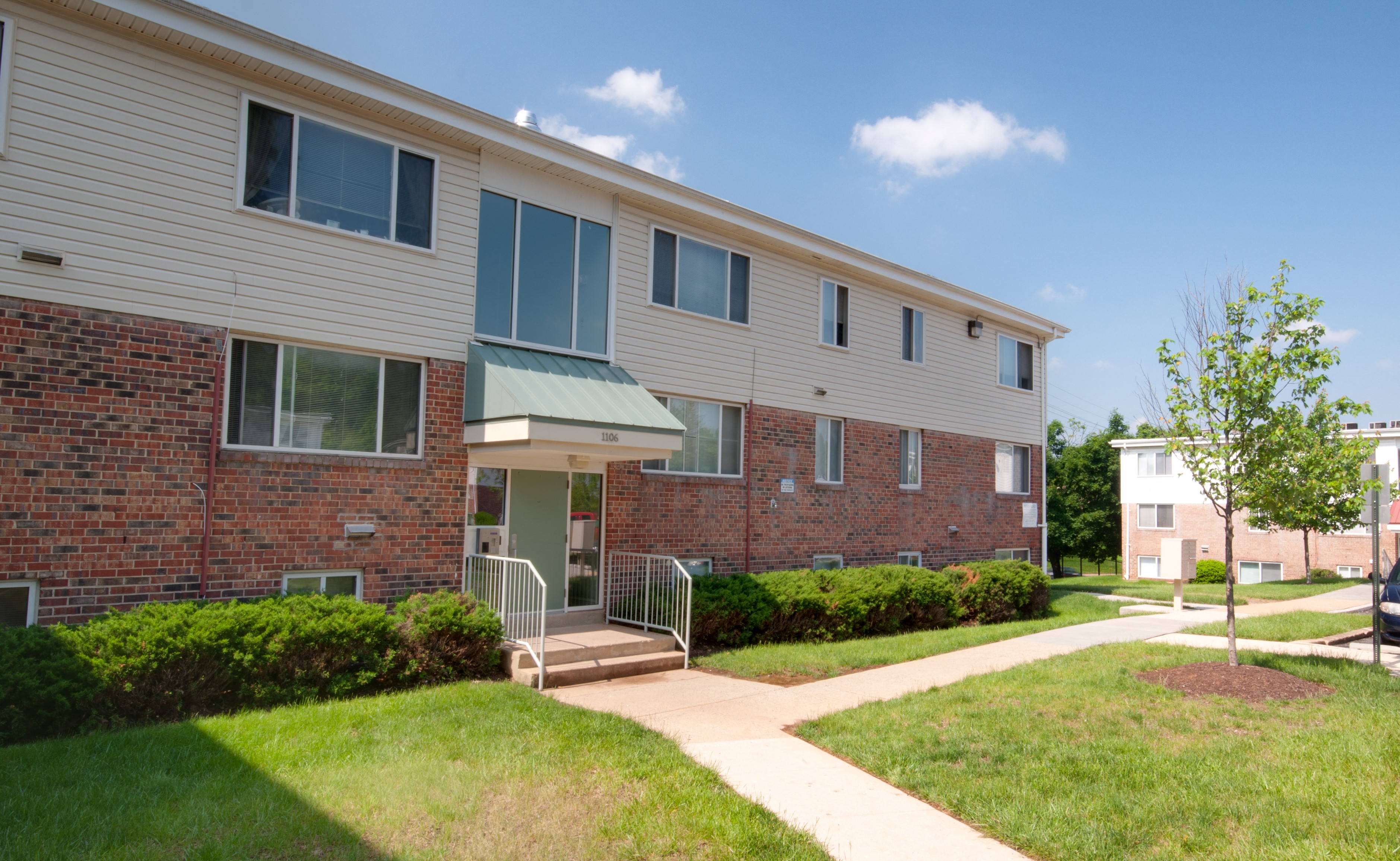 a brick and white apartment building with a walkway and grass