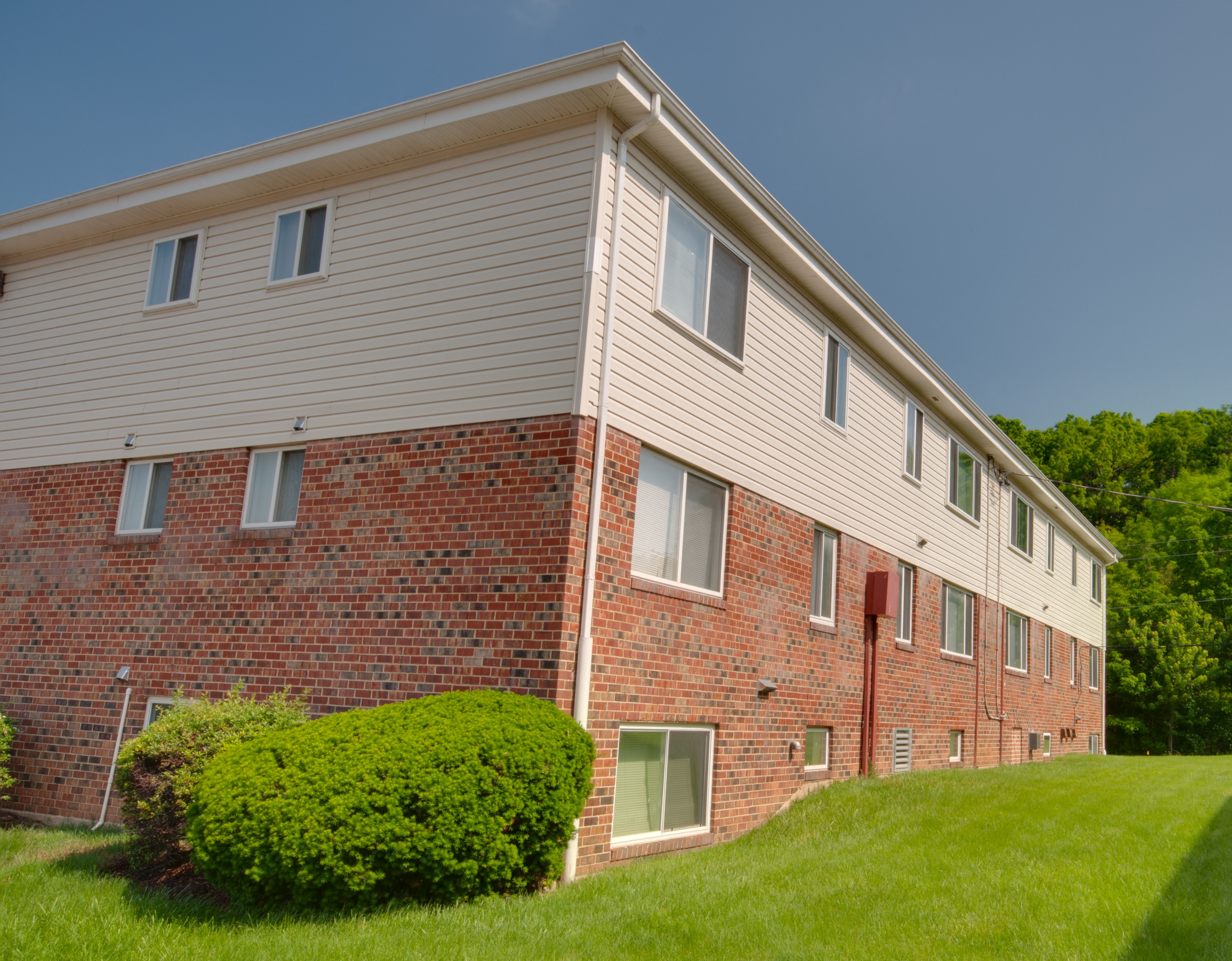 a brick building with white siding and a green lawn
