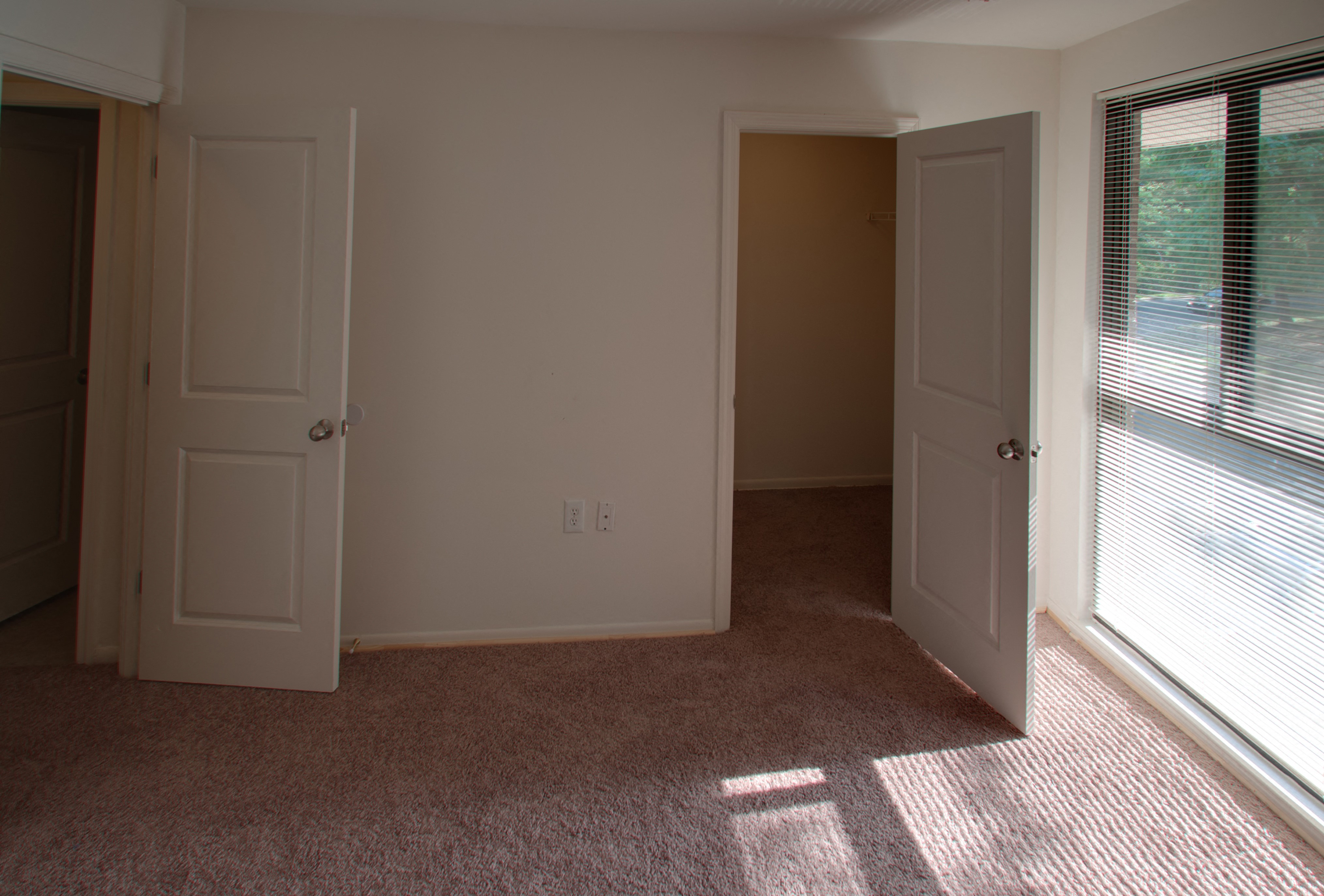 an empty bedroom with a window and two doors