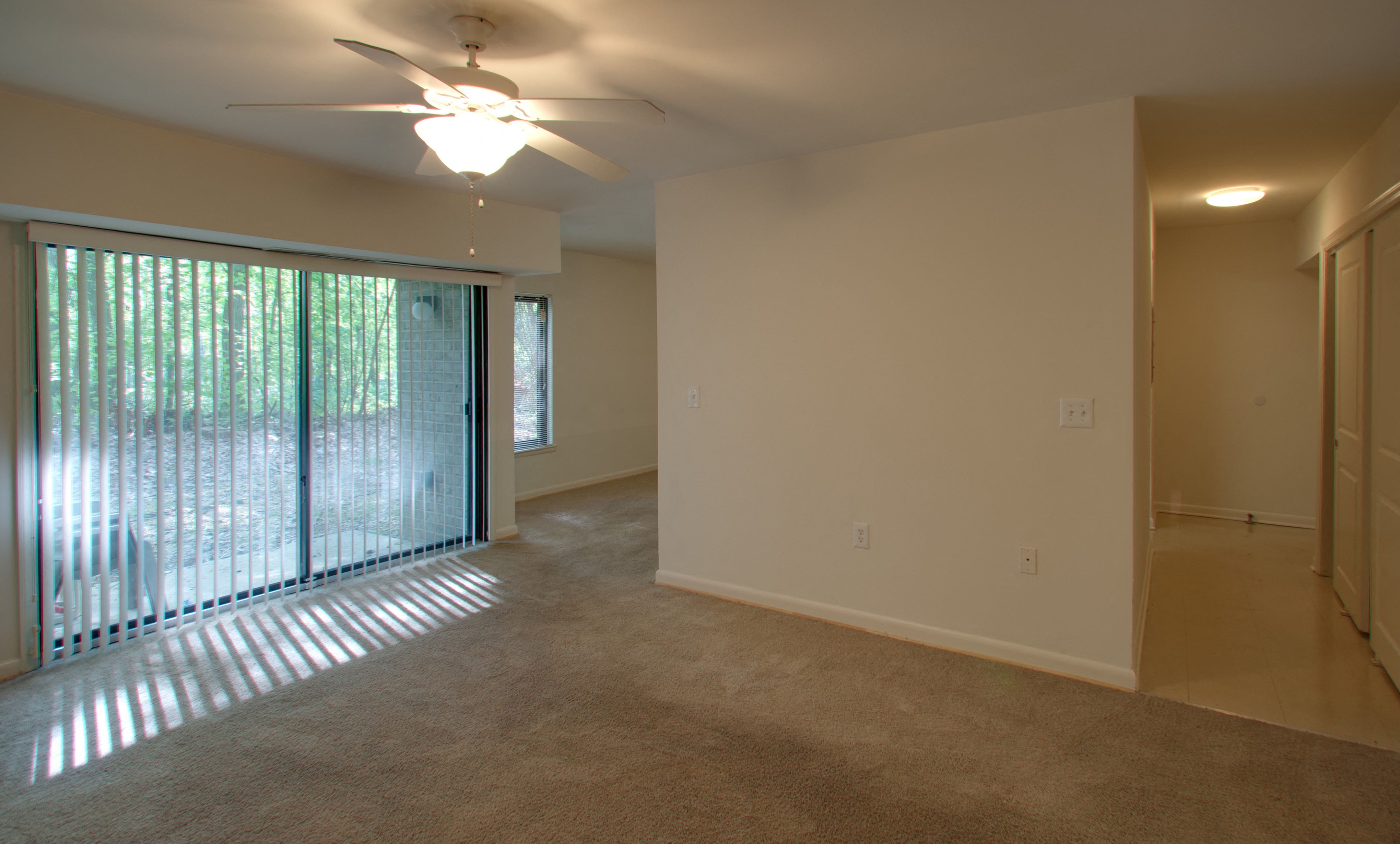 an empty living room with a large window and a ceiling fan